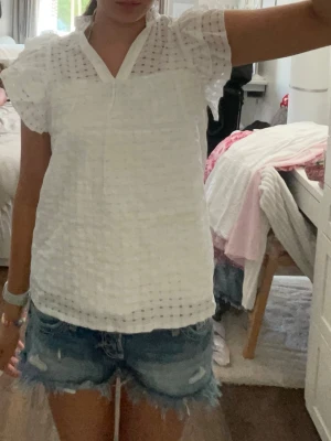Vit blus med v-ringning och struktur - Säljer en vit blus med v-ringning och korta ärmar. Blusen har ett strukturerat tyg med diskret rutmönster och luftig känsla. Perfekt till jeansshorts eller kjol för en fräsch look. Passar för 12-15 år