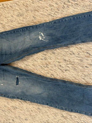 LTB Blå slitna jeans med hål - Säljer ett par blå jeans med slitningar och hål på benen. Jeansen har en klassisk femficksmodell, knappar i gylfen och en tvättad look med ljusa partier. Perfekta för en avslappnad och trendig stil.