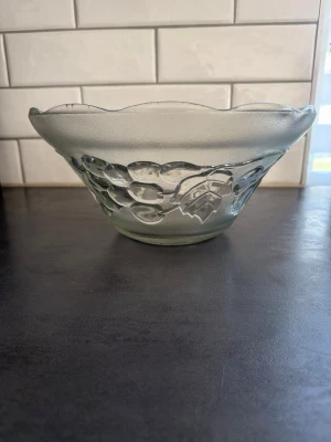 Transparent glasskål med druvmotiv - En rund skål i transparent glas med vågig kant och detaljerat druv- och bladmönster runt om. Perfekt som fruktskål eller till servering. Tillverkad i tjockt glas och har ett klassiskt, dekorativt utseende. Diameter ca 30 cm, ca 15 cm höjd.