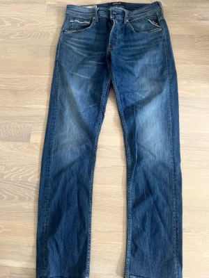 Blå raka jeans från Replay - Snygga blå jeans från Replay GROVER med klassisk femficksmodell och raka ben. Jeansen har en mörk tvätt med lätt slitna detaljer och tydliga sömmar. Perfekta för en avslappnad och trendig look.