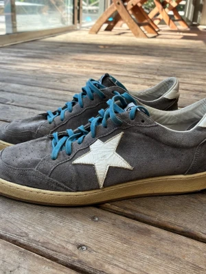 Golden Goose grå sneakers - Snygga äkta Golden goose sneakers i mocka med blå snören. Storlek 42 (passar som 43-43.5). Mycket fint skick, använda varsamt. Hör gärna av dig vid frågor! :)