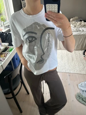 Trendig T-shirt från Zara - Säljer en vit t-shirt med ett stort abstrakt ansikte tryckt i svart och grått på framsidan. T-shirten har korta ärmar och en avslappnad passform. Perfekt för dig som gillar konstnärliga prints och en chill stil.