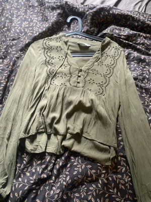 Olivgrön blus från Stradivarius XS - Supersöt olivgrön blus från Stradivarius i storlek XS. Blusen har långa ärmar, broderade detaljer och knappar framtill. Tillverkad i ett lätt, luftigt tyg som ger en avslappnad och trendig look. Perfekt att styla med jeans eller kjol.