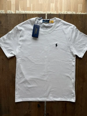Vit t-shirt från Polo Ralph Lauren - Klassisk vit t-shirt från Polo Ralph Lauren med rund halsringning och broderad logga på bröstet. Tillverkad i mjuk bomull och har en normal passform. Perfekt för en clean och stilren look.
