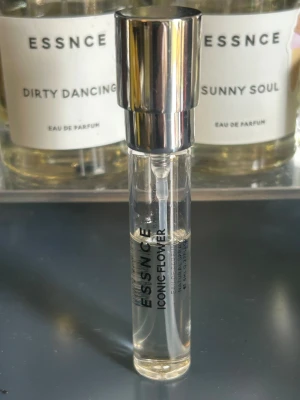 ESSNCE Iconic Flower parfym - Transparent glasflaska med silvrig spraykork från ESSNCE. Doften heter Iconic Flower och flaskan har en smal, cylinderformad design. Perfekt att ha med i väskan för en fräsch touch när som helst.