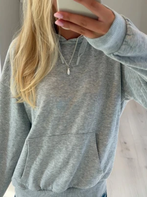 Hoodie - En ljusgrå hoodie med huva och dragsnören. Hoodien har en stor magficka framtill och ribbade muddar vid ärmslut och nederkant. Perfekt för en avslappnad och chill stil. 