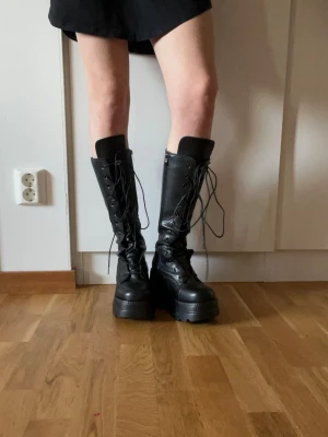Svarta höga platåstövlar - Säljer ett par svarta höga stövlar med chunky platåsula och snörning hela vägen upp. Stövlarna är i ett glansigt skinnliknande material och har en edgy look. Nypris 899