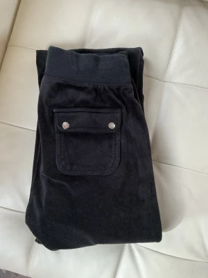 Svarta Juicy coutoure mjukisbyxor i velour - Säljer ett par svarta mjukisbyxor i mjuk velour med dragsko. Byxorna har raka ben och fickor med silverfärgade knappar. Perfekta för chill dagar eller när du vill vara extra bekväm.