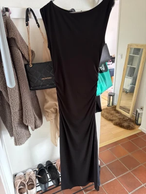 Svart långklänning med slits - Snygg svart långklänning med slits på sidan och enkel, stilren design. Klänningen har en rak passform och är ärmlös, vilket ger en elegant och tidlös look. Perfekt för dig som vill ha en klassisk och chic outfit.