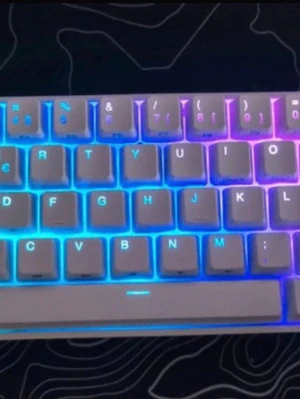 Kompakt mekaniskt tangentbord RGB - Snyggt kompakt mekaniskt tangentbord med vit plastdesign och RGB-belysning som lyser i flera färger. Tangentbordet har nordisk layout och ansluts med USB-kabel. Perfekt för gaming eller skrivbordssetup där du vill ha stilren look och cool belysning.