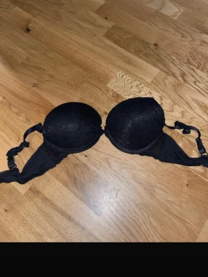 Svart push-up bh med spetsdetaljer - Snygg svart push-up bh med vadderade kupor och spetsdetaljer framtill. Justerbara axelband och hakknäppning bak. Perfekt för dig som vill ha extra stöd och en feminin look. Materialet är mjukt och bekvämt mot huden.
