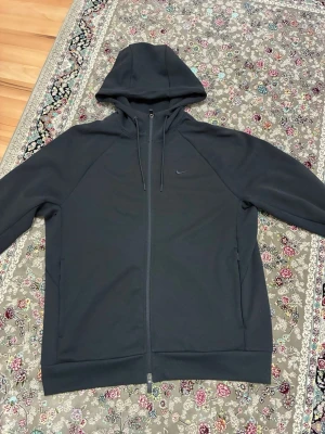Svart zip hoodie från Nike - Säljer en svart hoodie från Nike med dragkedja framtill och justerbar huva med snören. Hoodien har diskret Nike-logga på bröstet, långa ärmar och ribbade muddar. Perfekt för en avslappnad och sportig stil.