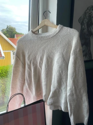 Vit stickad tröja med rund hals - Mysig vit stickad tröja med rund halsringning och långa ärmar. Tröjan har en avslappnad passform och ribbade muddar vid ärmslut och nederkant. Perfekt för kyliga dagar och enkel att matcha med olika outfits.