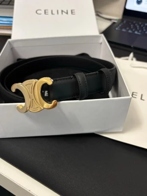 Svart bälte  - Snyggt svart bälte med ikoniskt guldspänne i metall. Bältet är gjort i slätt skinn och har en stilren, klassisk design som passar till många olika looks. Perfekt accessoar för att lyfta din outfit.