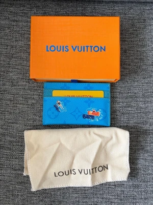 Lv korthållare - Säljer en blå korthållare från Louis Vuitton med lekfullt motiv av simmande personer och en röd båt. Tillverkad i tåligt läder med flera kortfack. Kommer med original ask och tygpåse. Perfekt för dig som vill ha något unikt och färgglatt i fickan.