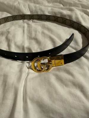 Gucci reversible bälte (Marmont thin belt) - Snyggt Gucci bälte med guldfärgat GG-spänne. Bältet är reversibelt så du kan ha bältet på 2 olika sätt, antingen så den svarta sidan syns, eller den andra sidan (se bild). Bältet har flera hål för justerbar passform och är gjort i skinn. Själva gucci märket är lite slitet men inget som är jättemärkvärdigt. Ordinariepriset är 4550kr.
