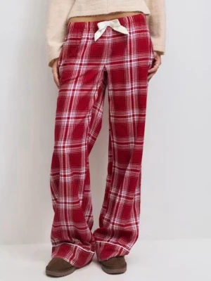 Rödrutiga pyjamasbyxor med rosett - Mysiga pyjamasbyxor i rött och vitt rutmönster med breda ben och en vit rosett i midjan. Byxorna har resår i midjan och är tillverkade i mjukt tyg, perfekta för chillkvällar hemma.