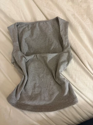 Grå ärmlös linnetopp - Säljer en enkel och stilren grå linnetopp i mjukt material. Toppen är ärmlös med rund halsringning och har en slim passform som sitter snyggt på kroppen. Perfekt att matcha med jeans eller kjol för en clean look.