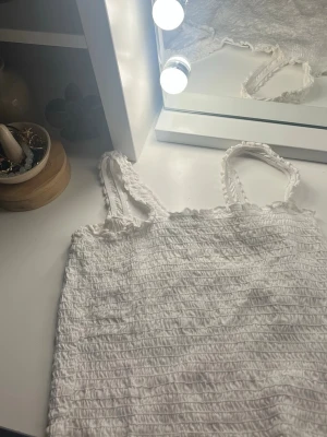 Vit smockad linnetopp - Säljer en söt vit linnetopp med smockad struktur och tunna axelband. Toppen har en stretchig passform och volangkant upptill för en gullig touch. Perfekt till sommaren och enkel att matcha med jeans eller kjol. Org pris 99,9😽😽💓