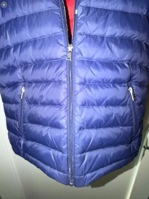 Mörkblå dunjacka från Polo Ralph Lauren - Snygg mörkblå dunjacka från Polo Ralph Lauren med röd insida och broderad logga på bröstet. Jackan har dragkedja framtill, två fickor med dragkedja och quiltad design. Perfekt för jacka för hela året och riktigt skön att bära. Det finns ett litet hål och en lagning som man ser på bilden! Storleken är 18-20 år vilket motsvarar S och XS. Den är äkta!!!