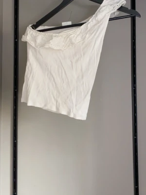 Vit oneshoulder topp med volang - Säljer en vit oneshoulder topp med volangdetalj längs axeln. 