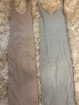 Två långa ribbade klänningar - Säljer två långa klänningar, en i beige och en i ljusgrå. Båda är ärmlösa med smala axelband och har en ribbad struktur. Perfekta för sommaren och kan stylas på många olika sätt.