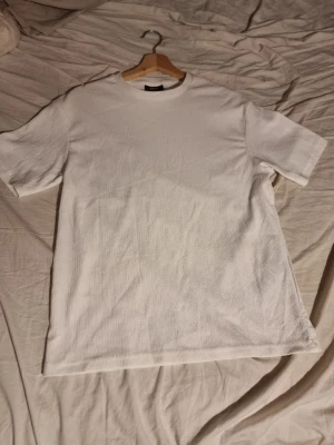 Vit basic t-shirt i bomull - INSTABOX!!! Klassisk vit t-shirt med rund hals och korta ärmar. Tillverkad i mjuk bomull med diskret textur i tyget. Perfekt att matcha med jeans eller shorts för en clean och enkel stil.