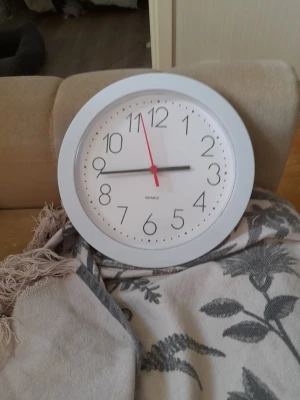 Vit rund väggklocka - Stilren rund väggklocka i vitt med tydliga svarta siffror och visare. Klockan har en enkel design och passar bra i de flesta rum. Tillverkad i plast och har en klassisk kvartsur-mekanism.