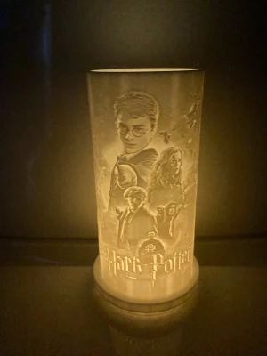 Harry Potter ljuslykta cylinder - Säljer en cylinderformad ljuslykta med Harry Potter-motiv. Lyktan är vit och har detaljerade porträtt av karaktärer från filmerna ingraverade i ytan. Passar perfekt som dekoration för fans av serien och ger ett mysigt sken när den är tänd. Med värme ljus hänger med