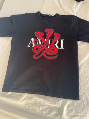 t-shirt med röd orm - Säljer en svart t-shirt med ett stort tryck av röda ormar och vit logga på bröstet. T-shirten har klassisk passform och rund hals. Perfekt för dig som vill sticka ut med en unik design. Storlek L
