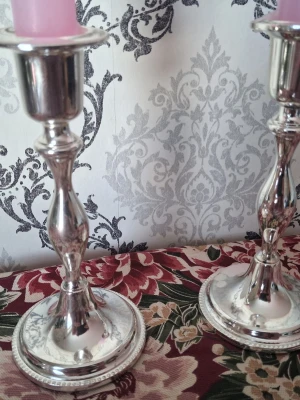 Två silverfärgade ljusstakar - Säljer två stilrena ljusstakar i silverfärgad metall med klassisk, svängd form. Passar för vanliga stearinljus och har en blank yta som ger en elegant känsla. Perfekta som dekoration på bord eller hylla.