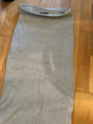 Ljusgrå ribbad midikjol - En enkel och stilren ljusgrå midikjol med ribbad struktur. Kjolen har en rak passform och är gjord i ett mjukt, stretchigt material som sitter bekvämt. Perfekt att matcha med en crop top eller hoodie för en avslappnad look.