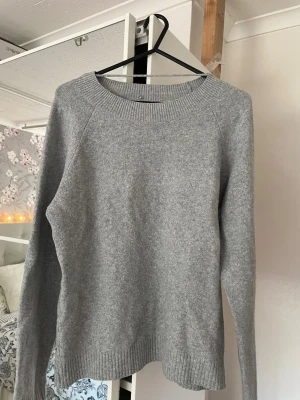 Grå stickad tröja från Vero Moda - Mysig grå stickad tröja från Vero Moda med rund halsringning och ribbade muddar vid ärmslut och nederkant. Perfekt för lager-på-lager och enkel att matcha med jeans eller kjol. Materialet känns mjukt och bekvämt.
