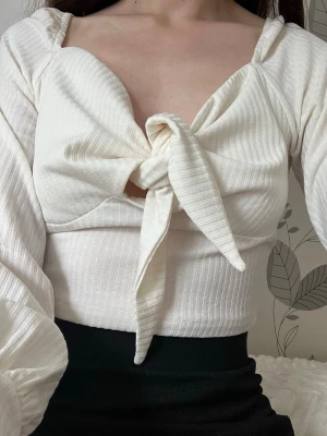 Vit ribbad topp med knyt framtill - Vit ribbad topp med långa puffärmar och knytning framtill. Toppen har en croppad passform och en lätt v-ringad urringning 😊