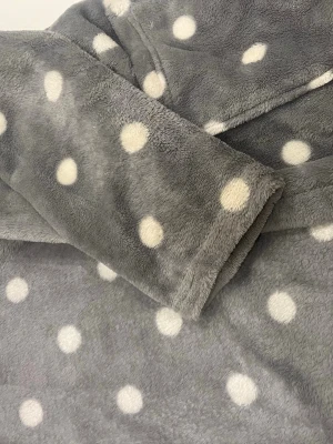 Grå morgonrock med vita prickar - Supermjuk och fluffig morgonrock i grått med vita prickar. Utsidan har ett mysigt fleece-tyg och insidan är fodrad med vit, lurvig pälsimitation. Perfekt för att chilla hemma och hålla sig varm.