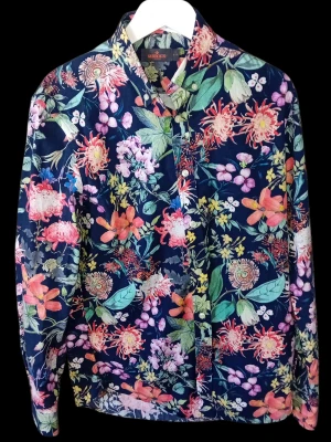 Blommig herrskjorta från Morris i strl S 37/38 - Säljer en långärmad skjorta med färgstarkt blommigt mönster i rosa, orange, grön och gul på mörkblå botten. Skjortan har klassisk krage och knappar framtill. Perfekt för dig som vill sticka ut med en unik och livlig stil.