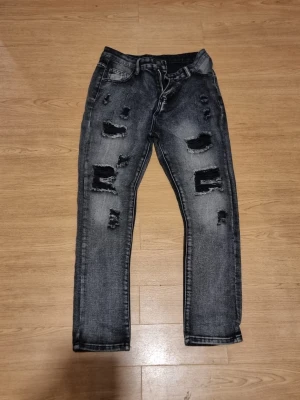 Gråa jeans med raka ben - INSTABOX!!! Säljer ett par gråa  jeans med hål framtill. Jeansen har raka ben, klassisk femficksmodell och tydliga slitdetaljer för en trendig look. Perfekta för dig som gillar streetstyle och vill sticka ut.