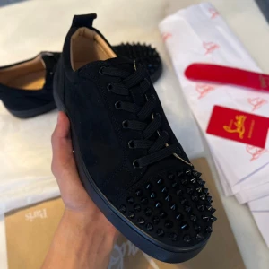 Svarta Loubs med nitar - Svarta sneakers i mocka med rund tå och snörning. Skorna har svarta nitar över hela tån för en edgy look och platt sula. Insidan är beige och materialet ser lyxigt ut. Perfekta för dig som vill sticka ut.