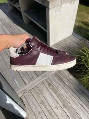 Vinröda Valentino Flycrew  - Storlek 39 passar 39/40 Snygga vinröda sneakers från Valentino med vita detaljer och matchande vinröda skosnören. Skorna är låga och har en klassisk siluett i läder med vit sula och diskret Valentino-logga på plösen. Perfekta för dig som vill ha en stilren och exklusiv look.