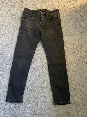 Svart/mörkgrå Jack&jones jeans  - Säljer ett par svarta  jeans med fem fickor och smal passform. Jeansen har klassisk design med bälteshällor och knappgylf. Materialet är stretchigt för extra komfort och sitter tight hela vägen ner. Perfekta till en avslappnad streetstyle-look. W29 L30