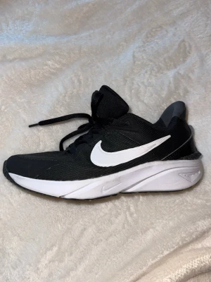 Svarta Nike sneakers med vit sula - Snygga svarta Nike sneakers med vit sula och vit swoosh-logga på sidan. Ovandelen är i meshmaterial för bra andningsförmåga och skon har klassisk snörning. Perfekta för dig som vill ha en sportig och stilren look.