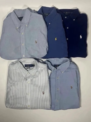 5 sljortor från Ralph Lauren - Säljer fem skjortor från Ralph Lauren i olika blå toner, inklusive en randig modell. Alla har knappkrage, broderad logga på bröstet och lång ärm. Perfekta för en clean och tidlös stil.