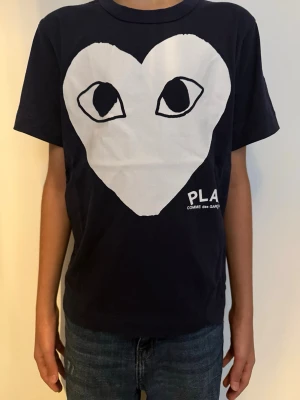 Svart t-shirt Comme des Garçons Play - Cool svart t-shirt från Comme des Garçons Play med stort vitt hjärta och ögon på bröstet. 