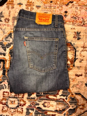 Levi's jeans  - Säljer ett par klassiska blå jeans från Levi's med smal passform och fem fickor. Jeansen har en snygg tvättad look, orange sömmar och Levi's ikoniska läderpatch bak i midjan. Perfekta till vardags för en avslappnad men stilren outfit.