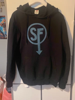 Svart hoodie med sally face logga - Säljer en svart hoodie med stor blå Sally face logga. Perfekt för dig som gillar streetwear och vill ha en skön och stilren tröja. Säljer på grund av att den tyvärr inte används. Har endast använts 2 eller 3 gånger 😊öppen för prisförslag 