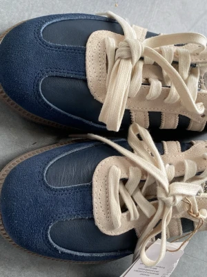 Adidas Samba blå och beige sneakers -  Adidas Samba sneakers i mörkblått och beige. Helt oanvända pga fel storlek så jag testar att sälja för att slippa skicka tillbaka. Köpt för 1800 kr men säljer för 1500, icke prutbart.