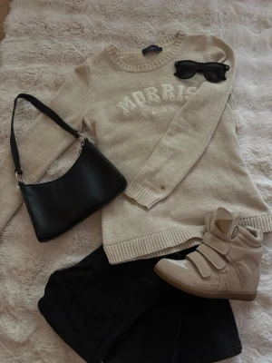 Beige stickad tröja från Morris Lady - Snygg beige stickad tröja från Morris Lady med rund halsringning och vit broderad logga framtill. Tröjan har långa ärmar och ribbade muddar vid ärmslut och nederkant. Perfekt för lager på lager och enkel att matcha med jeans eller kjol. Obs! Endast tröjan till salu!