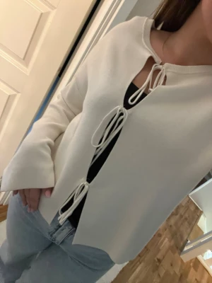 Vit cardigan med knytband - Trendig vit cardigan med tre knytband framtill. Långärmad och rak passform, perfekt att slänga över ett linne eller t-shirt. Mjuk och skön, passar till både jeans och kjol för en avslappnad look.