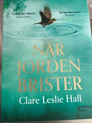 När jorden brister bok - Säljer romanen 'När jorden brister' av Clare Leslie Hall. Omslaget är turkost med guldfärgad text och en fågel som flyger över vatten. Boken är utgiven av Bokförlaget Forum och är i pocketformat. Perfekt för dig som gillar gripande berättelser om kärlek och hemligheter.