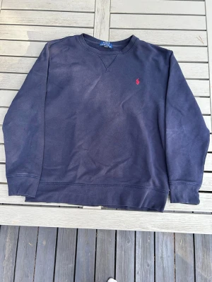 Mörkblå sweatshirt från Polo Ralph Lauren - Mörkblå sweatshirt från Polo Ralph Lauren med rund halsringning och den klassiska röda logotypen broderad på bröstet. Tröjan är väldigt lite använd och den köptes direkt från polo Ralph lauren! Skriv vid några funderingar.